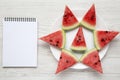 Sliced watermelon on white plate with blank notepad over white wooden background, top view. Royalty Free Stock Photo