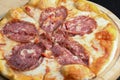 Sliced whole salami pizza on a rustic wooden board over black wooden table. Fast food, junk food concept. Royalty Free Stock Photo