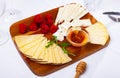 Slices of artisanal cheeses on wooden board with raspberries and honey