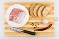 Bacon in plate, bread, knife, pepper, garlic on cutting board Royalty Free Stock Photo