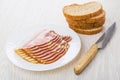 Slices of bacon in plate, stack of bread, kitchen knife