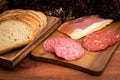 Slices of becon and salami on the brown wooden board.