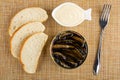 Slices of bread, bowl with mayonnaise, opened jar with sprats, fork on mat. Top view