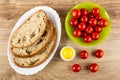 Slices of bread in white dish, bowl with fresh red cherry tomato, salt on wooden table. Top view