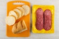 Slices of bread on cutting board, slices of sausage salami in package on wooden table. Top view Royalty Free Stock Photo