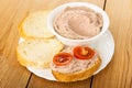 Slices of bread, liver pate in bowl, sandwich with liver paste and tomato in plate on table