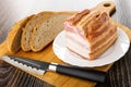 Bread, piece of smoked pork brisket in plate, knife on cutting board on wooden table Royalty Free Stock Photo