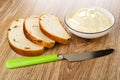 Slices of bread with raisin white bowl with creamy cheese knife on wooden table