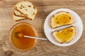 Slices of bread, spoon in bowl with honey, sandwiches from rich bread with raisin and honey in plate on wooden table. Top view