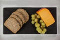 Slices of brown bread, grapes and gouda cheese on slate board Royalty Free Stock Photo