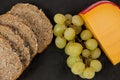 Slices of brown bread, grapes and gouda cheese on slate board Royalty Free Stock Photo