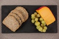 Slices of brown bread, grapes and gouda cheese on slate board Royalty Free Stock Photo