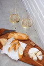 Slices of camembert cheese, baguette and two glasses of white wine on wooden board. White brick wall as background Royalty Free Stock Photo