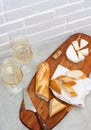 Slices of camembert cheese, baguette and two glasses of white wine on wooden board. White brick wall as background Royalty Free Stock Photo