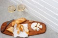 Slices of camembert cheese, baguette and two glasses of white wine on wooden board. White brick wall as background Royalty Free Stock Photo