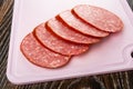 Slices of cervelat on pink cutting board on wooden table Royalty Free Stock Photo