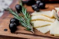 Slices of cheese, olives and rosemary on board