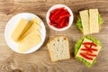 Slices of cheese in plate, bowl with sweet pepper, slice of bread, sandwiches with cheese, lettuce and pepper on table. Top view