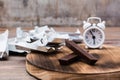 Slices of chocolate, a pile of empty wrappers and an alarm clock on a wooden table. Concept of eating sweet time and diet