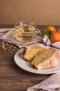 Slices of clementine cake with powdered sugar topping and cup of chamomile tea. Cake on a plate with fresh clementines on wooden