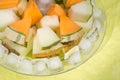 Slices different melon with ice on plate around green background. tasty sweet exotic fruit. close up