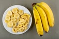 Slices of banana and banana chips in plate, bunch of banana on gray table. Top view