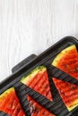 Slices of fresh grilled watermelon in grilling pan on a white wooden background, top view. Healthy organic summer fruit. Royalty Free Stock Photo