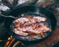 Slices of fried bacon in a pan. Food in a forest camp. Cooking on fire. Picnic in the nature. Grilled food on nature Royalty Free Stock Photo