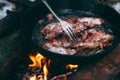 Slices of fried bacon in a pan. Food in a forest camp. Cooking on fire. Picnic in the nature. Grilled food on nature. Fork taking Royalty Free Stock Photo