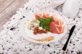 Slices of ham, walnuts and cheese on a plate. A knife and fork near a dish on a white stones background. Luxury dinner. Royalty Free Stock Photo