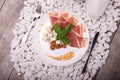 Slices of ham, walnuts and cheese on a plate. A knife and fork near a dish on a white stones background. Luxury dinner. Royalty Free Stock Photo