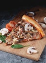 Slices of homemade Italian pizza on a chopping wooden board with mushrooms ham tomatoes cheese onions and herbs Royalty Free Stock Photo