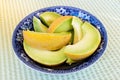 Slices of honeydew melon in a blue antique bowl isolated on green and white tablecloth.