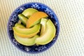 Slices of honeydew melon in a blue antique bowl isolated on green and white tablecloth from above.