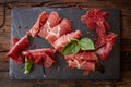 Slices of Italian prosciutto crudo or jamon with fresh basil leaves on a black background. Royalty Free Stock Photo