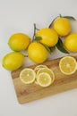 Slices of juicy lemons with leaves on a cutting wooden board and branches with lemon on a white background. Organic citrus fruits Royalty Free Stock Photo