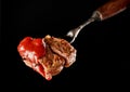 Slices of Medium rare grilled Steak Ribeye with ketchup on meat fork on black background. Juicy piece of meat on a fork Royalty Free Stock Photo