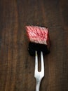 Slices of medium rare ribeye steak on meat fork on a dark wooden background