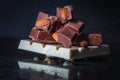 Slices of milk chocolate with almonds and tiles of white chocolate with hazelnuts on an old dark metallic background