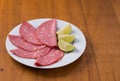 Slices of mortadella served with lemon on a white plate, on a wooden background Royalty Free Stock Photo