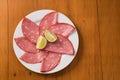 Slices of mortadella served with lemon on a white plate, on a wooden background. top view Royalty Free Stock Photo