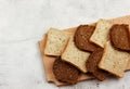 Slices of multigrain bread and rye bread on a wooden cutting board on a light gray background.