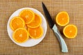 Slices of oranges in white plate, knife, two halves of orange on mat. Top view Royalty Free Stock Photo