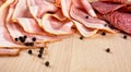 Slices of pink bacon and salami with black peppercorn on wooden