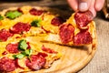 Slices of pizza with cheese and salami in hand on a wooden plate