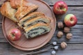 Slices of poppy seed pie on round wooden board with whole walnuts and red apples.