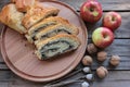 Slices of poppy seed pie on round wooden board with whole walnuts and red apples.