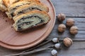 Slices of poppy seed strudel on round wooden board with whole walnuts.