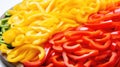 Slices of red and yellow bell pepper on a wooden plate. Closeup view. Sliced pepper background