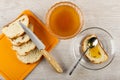 Slices of rich bread with raisin, knife on cutting board, bowl with liquid honey, spoon on sandwich with honey in saucer on table